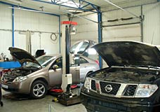 Az Alfa Autóház Szerviz raktárról vagy beszerzés útján minden minőségi alkatrészt biztosít a megrendelőnek. A képen: két autó a műhelyben javítás közben.